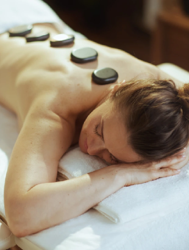 A woman laying on top of a bed with hot stones on her back.